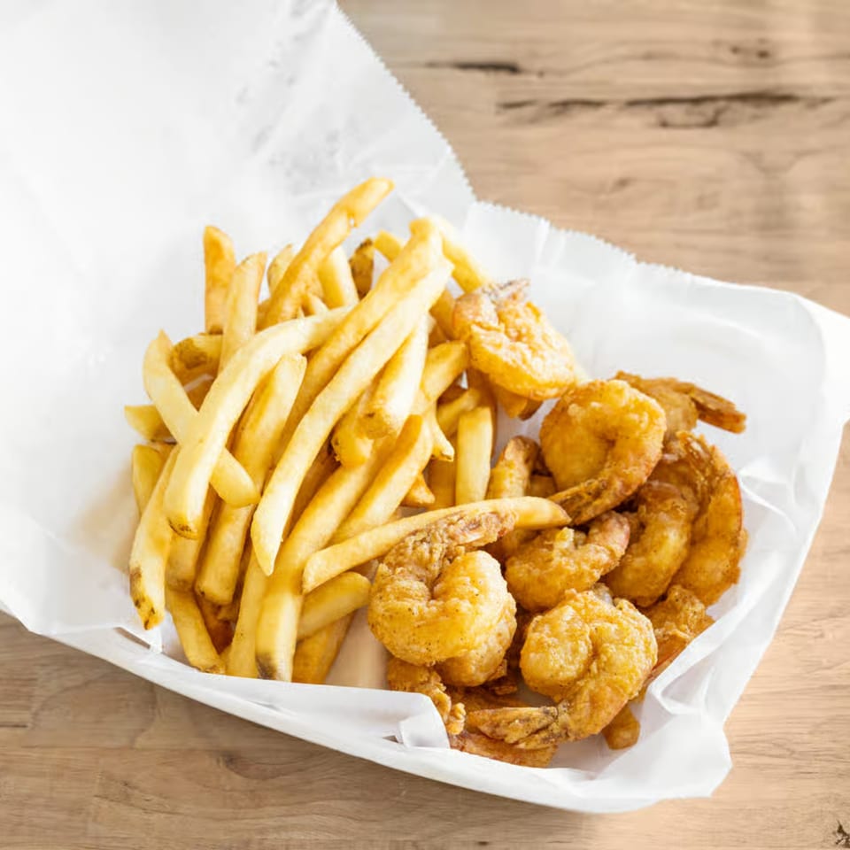 Golden-brown fried shrimp and crispy french fries served in a white paper-lined basket on a wooden table.