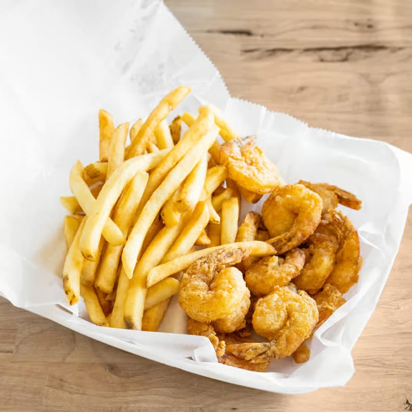 Golden-brown fried shrimp and crispy french fries served in a white paper-lined basket on a wooden table.