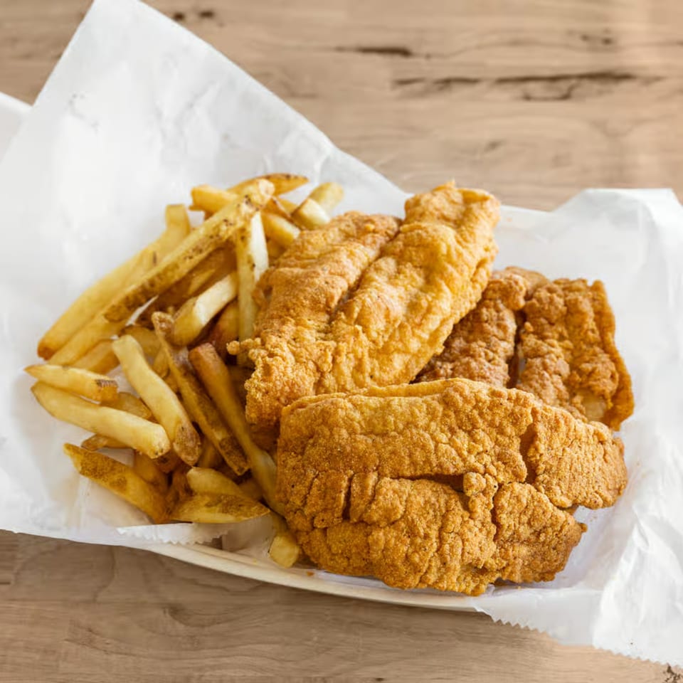 Crispy fried fish fillets and golden french fries served on white paper in a basket.