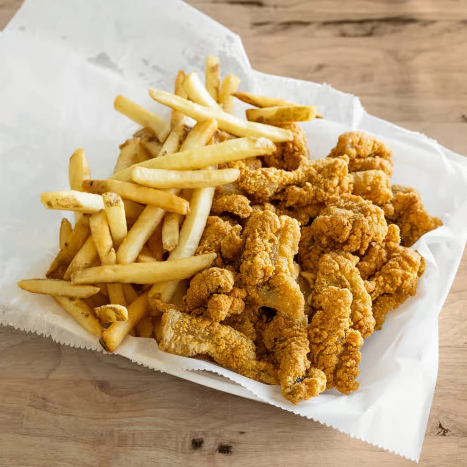 A serving of crispy fried fish and golden french fries on white paper, on a wooden table.