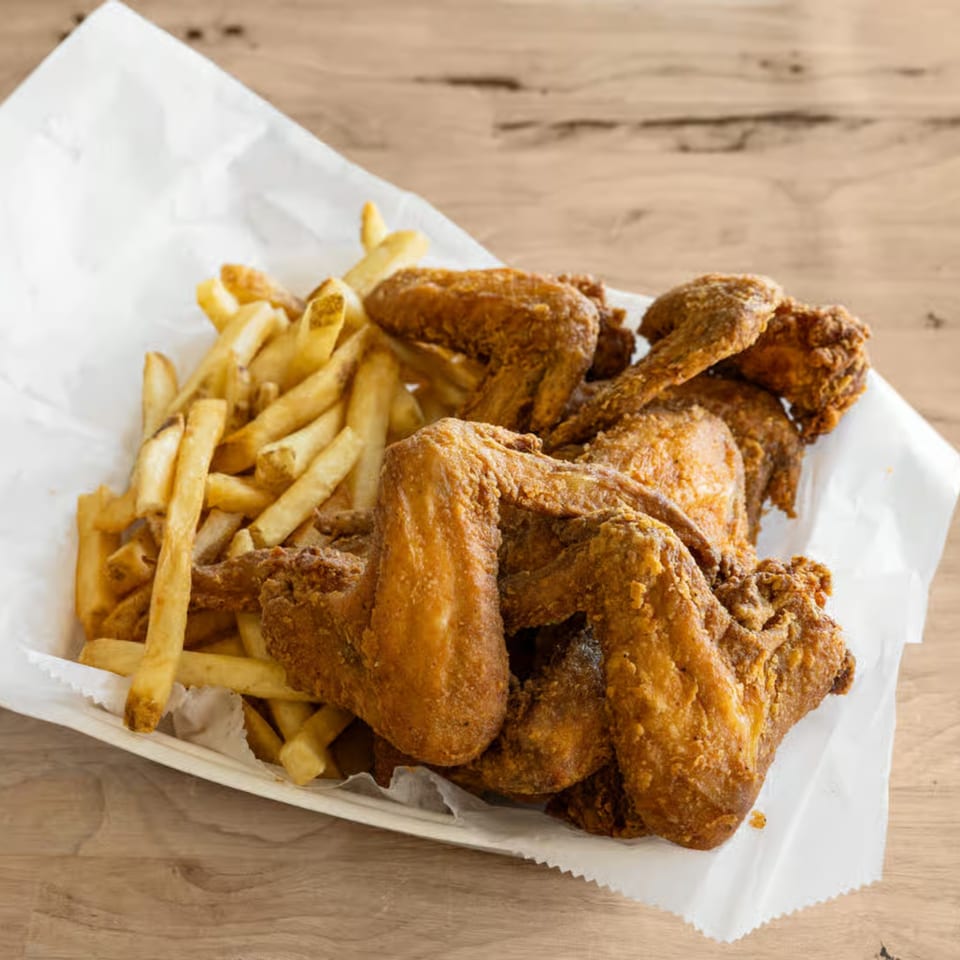Golden-brown fried chicken wings and crispy french fries served in a paper-lined basket.